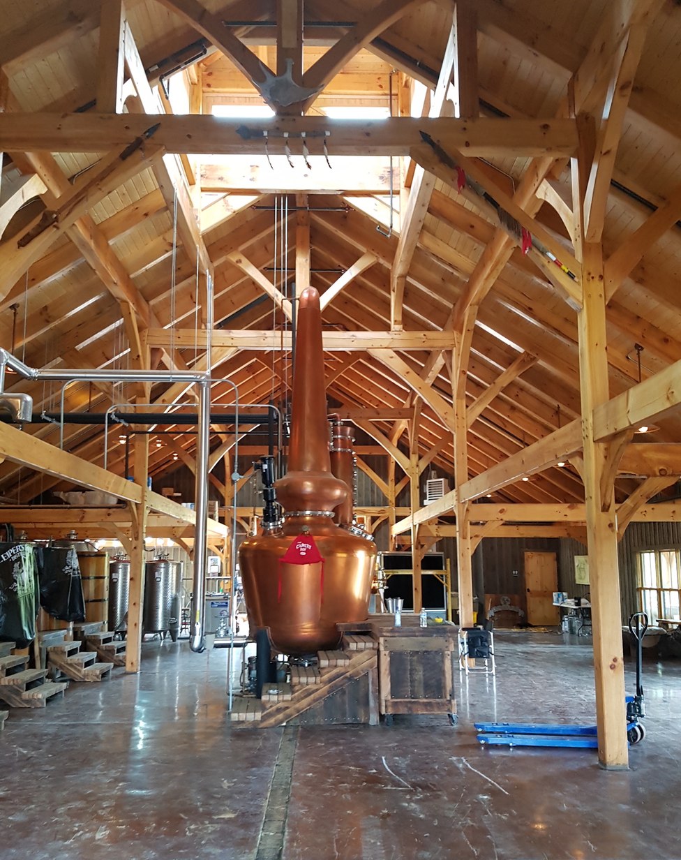 Copper pot still standing beneath exposed timber frame trusses in the stillhouse