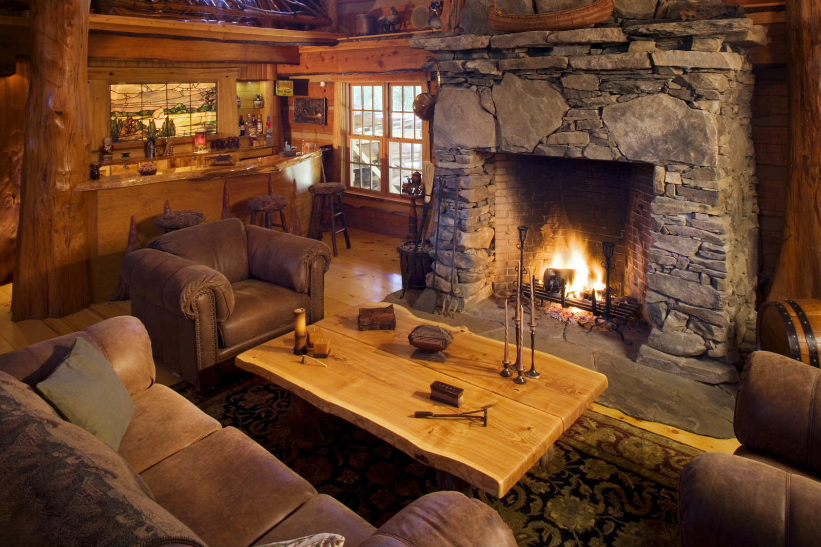 Log-lounge fireplace corner with dry-stack stone hearth, leather club chairs, and cypress bark-on posts