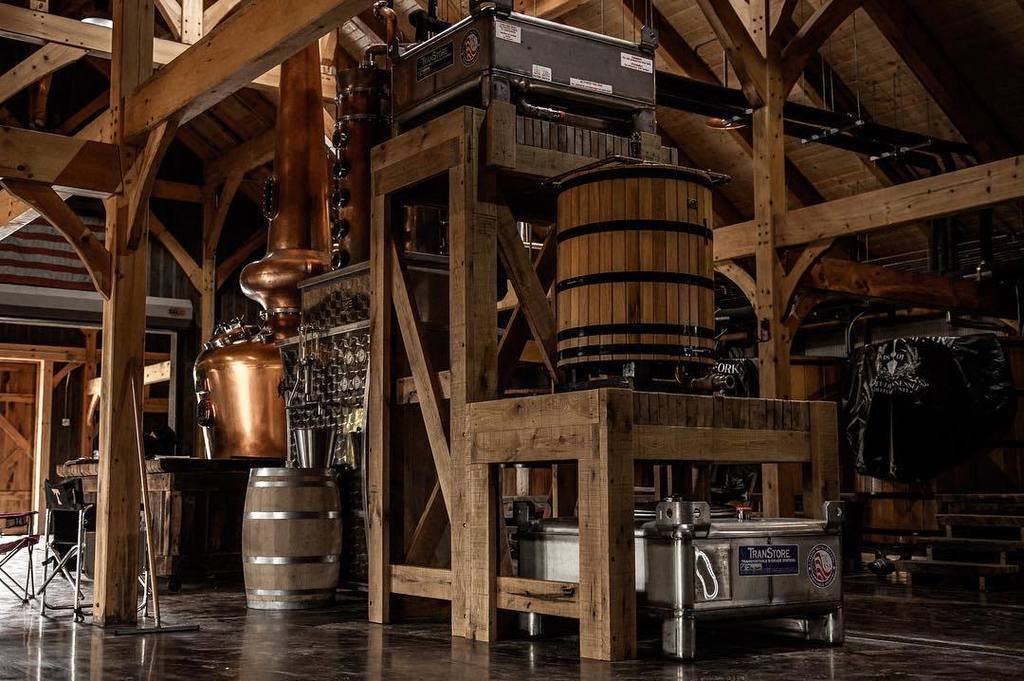 Copper still and mash tuns framed by heavy timber posts and a fermenter platform